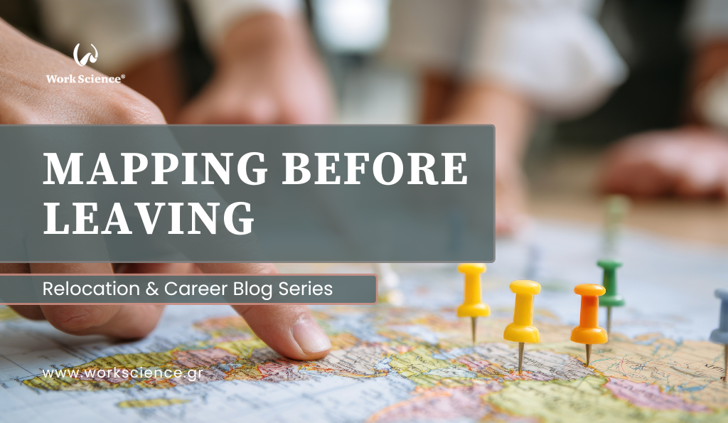 The image is a close-up of a person's hand pointing to a location on a physical map, which is marked with several colorful pushpins (yellow, orange, green, and gray).